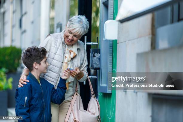 senior woman and her grandson are using an atm machine. - community investment stock pictures, royalty-free photos & images