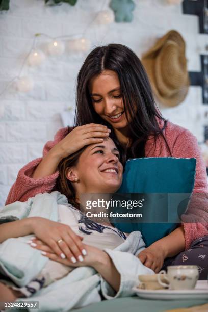 jovem mulher abraçando sua namorada na cama enquanto eles estão desfrutando chá - slumber party - fotografias e filmes do acervo