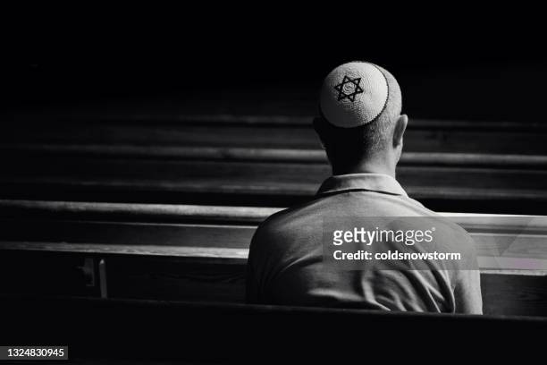 young jewish man wearing skull cap praying inside synagogue - judaism stock pictures, royalty-free photos & images
