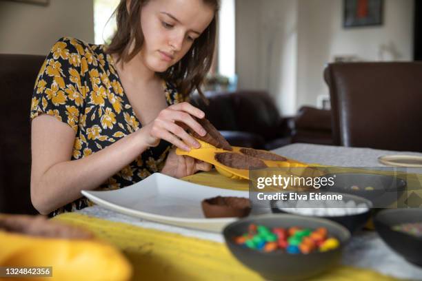 teenage girl removing moulded chocolate easter eggs from silicone moulds at a dining table in preparation for decorating them - shaping future stock-fotos und bilder