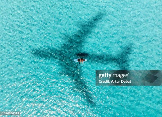 aerial view of paddle board guy in paradise water beach with airplane shadow. - 新常態 概念 個照片及圖片檔