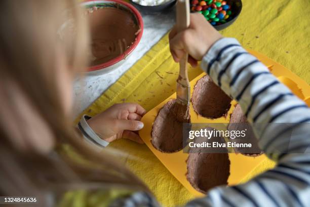 high angle view of child painting melted chocolate onto a silicone mould with a pastry brush in preparation for making homemade easter eggs - shaping future stock-fotos und bilder