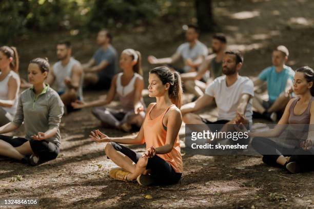 large group of athletes meditating on yoga class in nature. - zen stock pictures, royalty-free photos & images