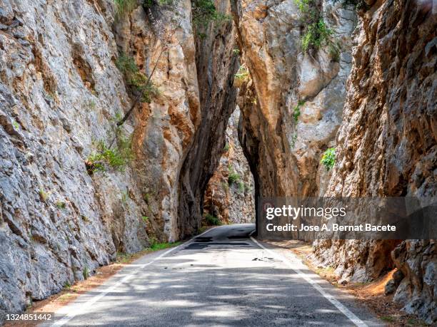 road going through a narrow natural tunnel between the rocks of a mountain in sa calobra, majorca island. - narrow stock pictures, royalty-free photos & images