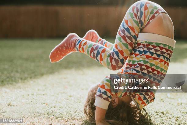 a little girl does a head-over-heel tumble in a sunny garden - flip stock-fotos und bilder