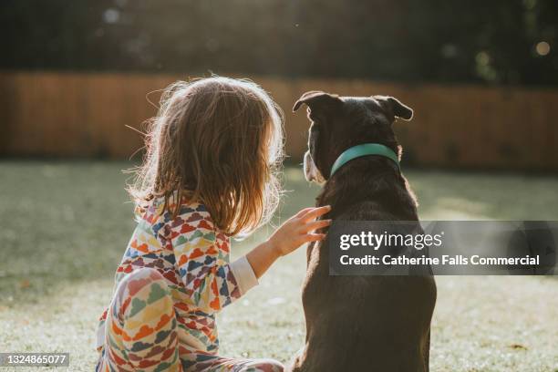 young girl sits beside an old black dog in a sunny garden - criança de escola primária imagens e fotografias de stock