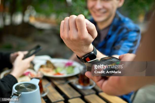 young couple paying with smart watch in a cafe - watch payment stock pictures, royalty-free photos & images