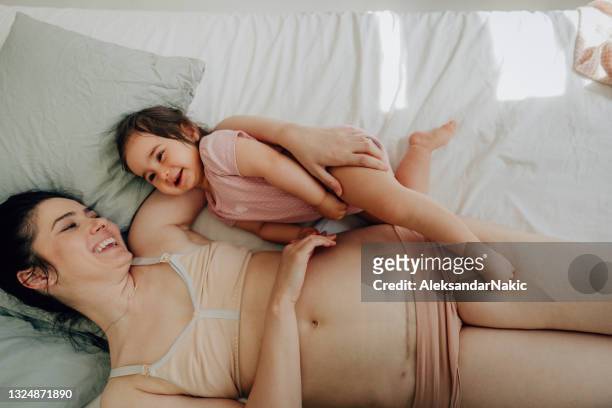 mutter mit c-sektion narbe und ihr baby auf dem bett liegend - pregnant belly stock-fotos und bilder