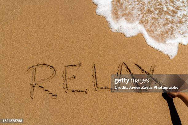 cropped hand writing "relax" in sand on beach - hand written letter ストックフォトと画像