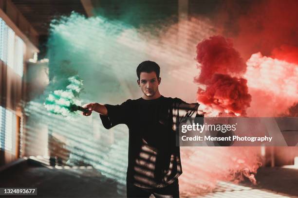 man holding colored smoke bomb and standing an abandoned warehouse - アクション映画 ストックフォトと画像