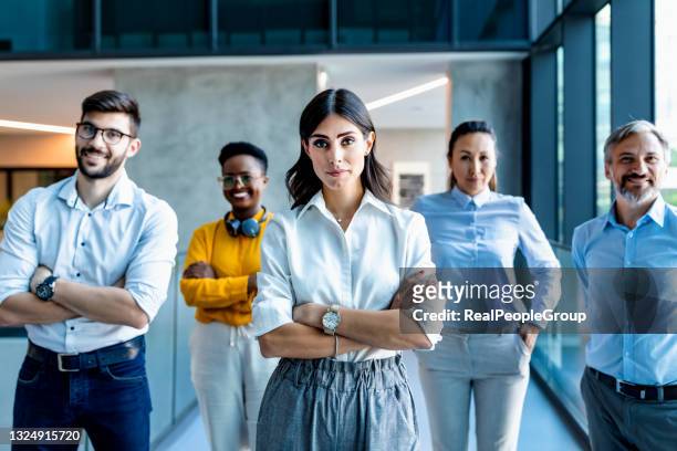 successful businesswoman smiling at camera while her colleagues standing behind him in office corridor - five people stock pictures, royalty-free photos & images