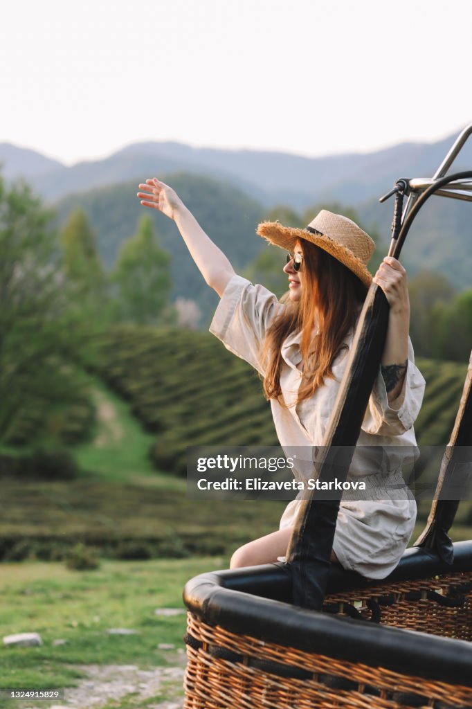 Beautiful happy free smiling cheerful young female tourist in casual clothes and sunglasses enjoys solitude traveling in local places among green tea plantations and fields in the mountains in nature in the summer