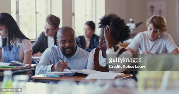 shot of a teacher assisting a struggling student with schoolwork in a classroom - professional childrens school stock pictures, royalty-free photos & images