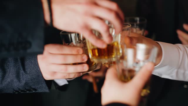 A group of guys of friends drink whiskey and clink glasses in the room. Close-up shooting