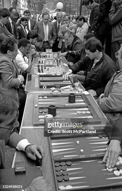 View along a row of folding tables on which pairs of men play backgammon and chess, watched by onlookers, in Liberty Plaza Park , New York, New York,...