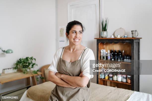 portrait of a beatician working at a spa sitting on table massage and looking away with crossed arms. - masseuse stock pictures, royalty-free photos & images