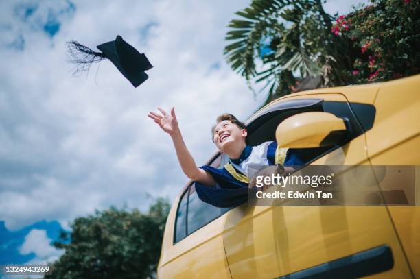 asian chinese young female with graduation gown throwing mortarboard cap in the air from driver seat of her car laughing - graduation celebration stock pictures, royalty-free photos & images