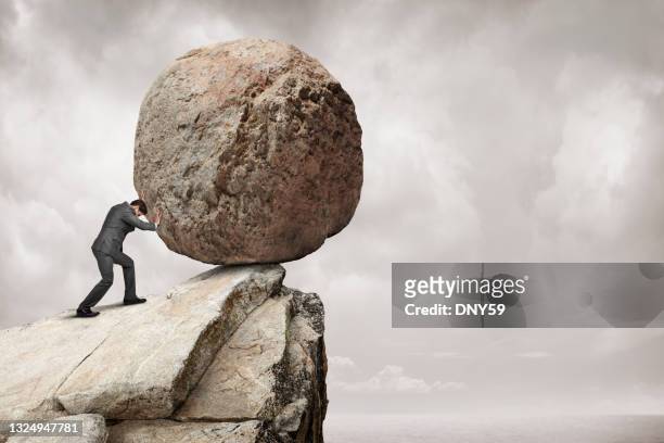 el hombre empuja una gran roca desde un acantilado - boulder rock fotografías e imágenes de stock
