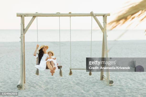 mother and baby daughter swinging on a big beautiful wooden swing on the beach - swinging stock pictures, royalty-free photos & images