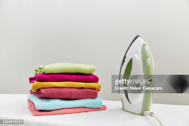 steam iron and folded clothes on ironing board - multi colored shirt foto e immagini stock