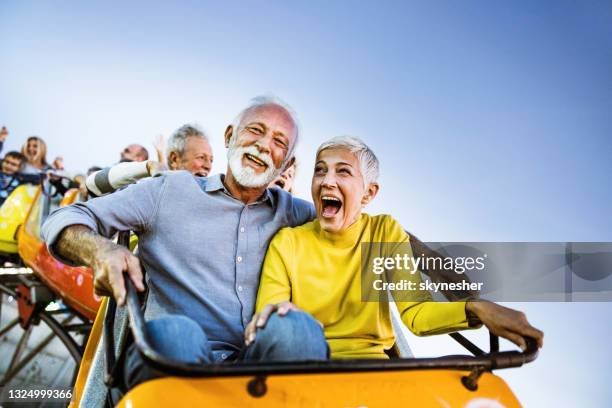 happy senior couple having fun while riding on rollercoaster at amusement park. - amusement park ride stockfoto's en -beelden