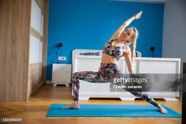 happy woman doing yoga at home in reverse warrior pose, looking at camera - low effort stock pictures, royalty-free photos & images