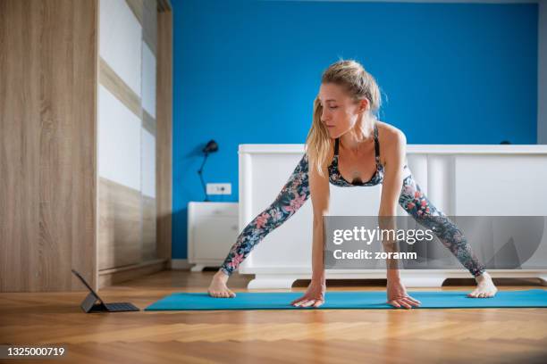 woman watching tutorial and doing yoga at home, half feet spread out intense stretch pose - older woman bending over stock pictures, royalty-free photos & images