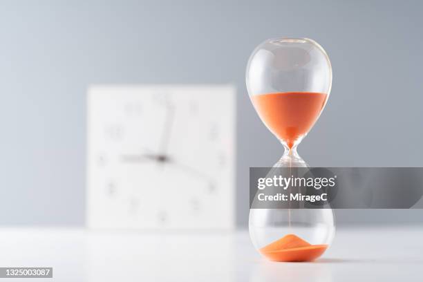 orange colored sand hourglass in front of clock - time clock stock pictures, royalty-free photos & images