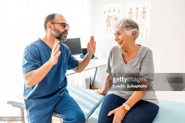 confident mature male chiropractor talks with new patient - physical therapist stock pictures, royalty-free photos & images