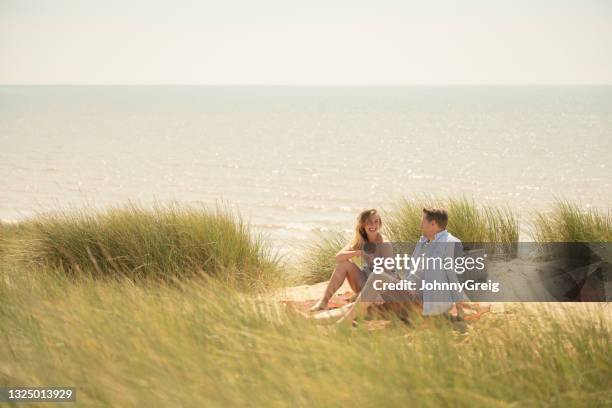 ビーチで毛布でリラックスした20年代と30年代の笑顔のカップル - camber sands ストックフォトと画像