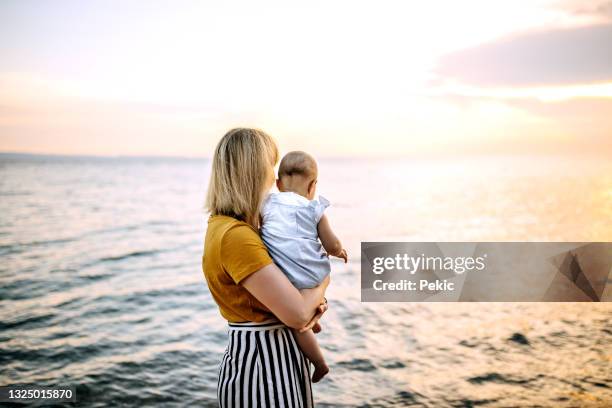 mother with cute little baby girl enjoying sunset on the beach - beautiful baby stockfoto's en -beelden