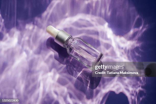 blank glass face serum bottle on purple background. - cosmetic bottle stockfoto's en -beelden