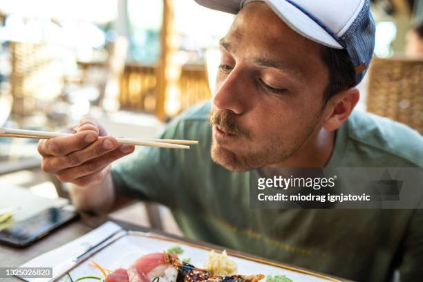 mann isst leckeres sushi im restaurant im freien - stäbchen stock-fotos und bilder