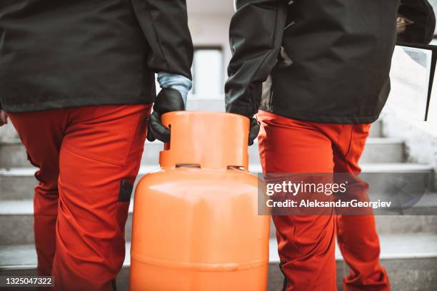 liquefied gas storage workers carrying gas cylinder on staircase - gas cylinder stockfoto's en -beelden