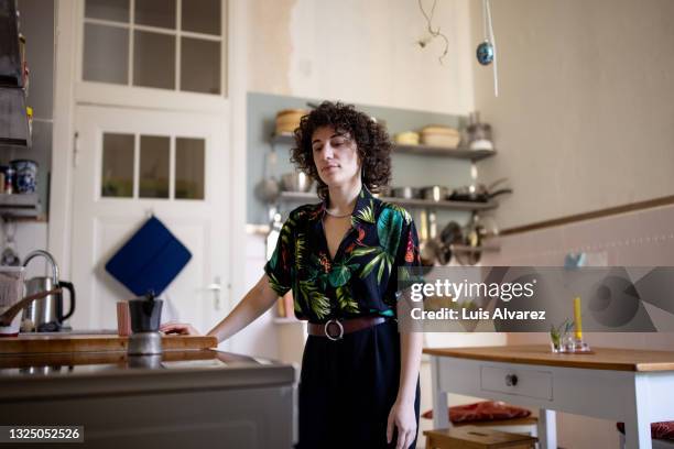 non-binary person watching coffee cooking on an electric stove - burner stove top stockfoto's en -beelden