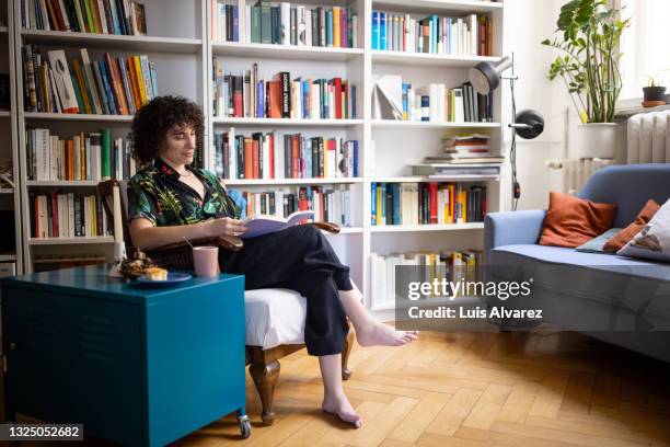 genderqueer person person reading a book at home - fashion woman floor cross legged stock pictures, royalty-free photos & images