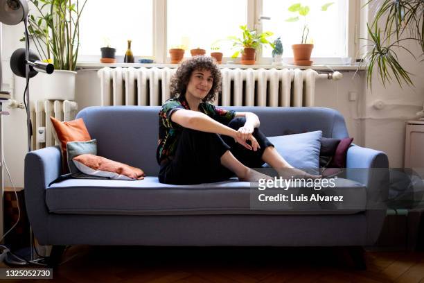 portrait of a non-binary person sitting on sofa at home - sitzen stock-fotos und bilder