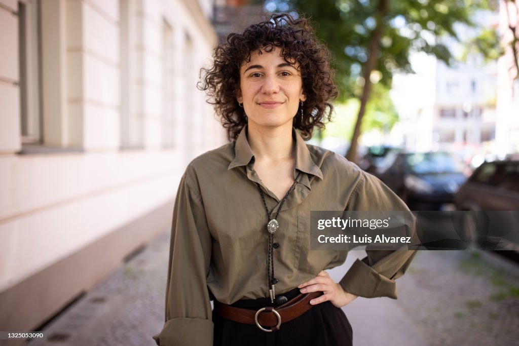 Confident non-binary person standing with hand on hip outdoors