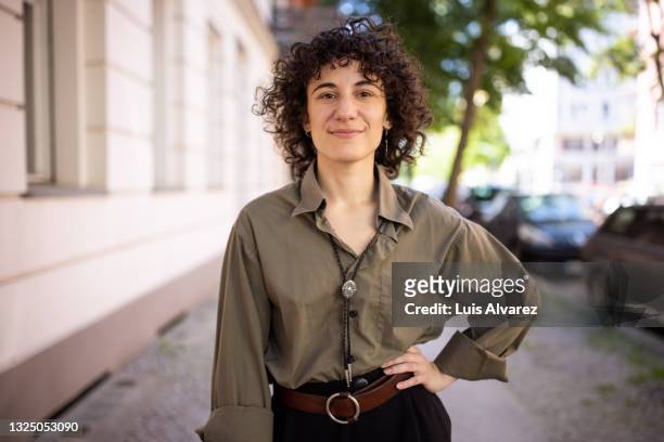 confident non-binary person standing with hand on hip outdoors - portretfoto stockfoto's en -beelden