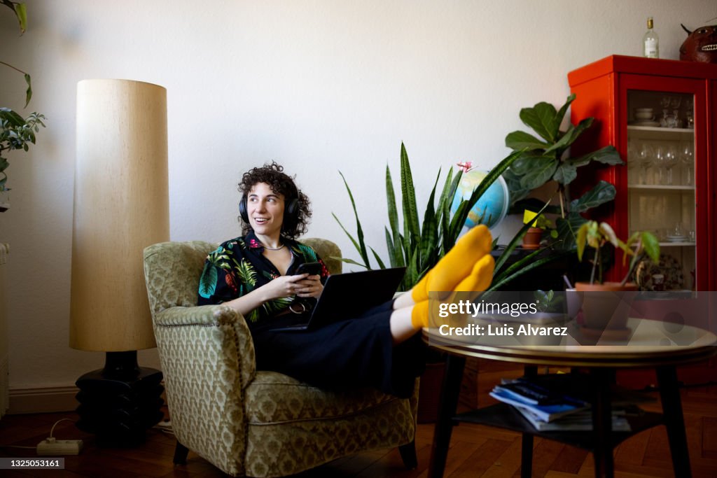 Non-binary person listening to music while working on laptop at home