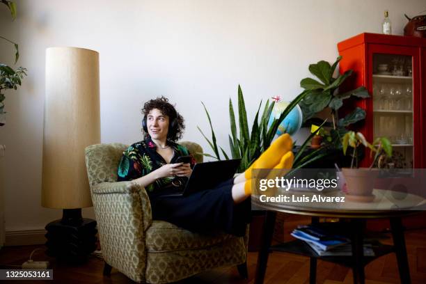 non-binary person listening to music while working on laptop at home - casual fashion imagens e fotografias de stock