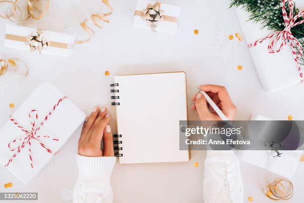 from above anonymous woman in knitted sweater making new year's goals in blank planner near christmas gifts and confetti on gray background. new year's celebration concept - new year resolution stock-fotos und bilder