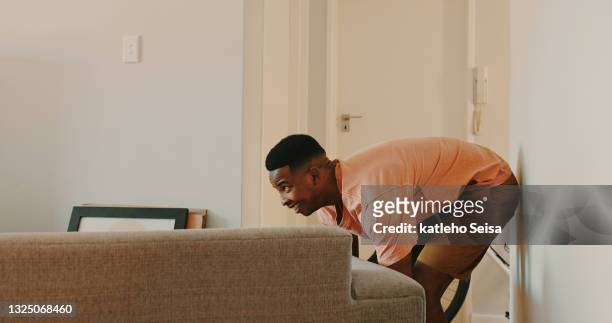 shot of a young man moving a couch at home - pushing stockfoto's en -beelden