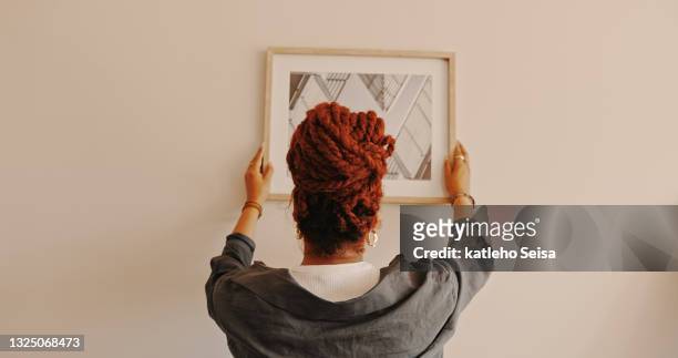 shot of a unrecognizable female hanging a painting at home - hanging stock pictures, royalty-free photos & images