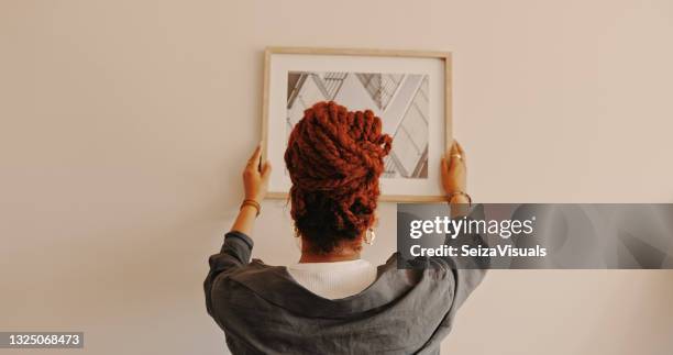 shot of a unrecognizable female hanging a painting at home - pendurar imagens e fotografias de stock
