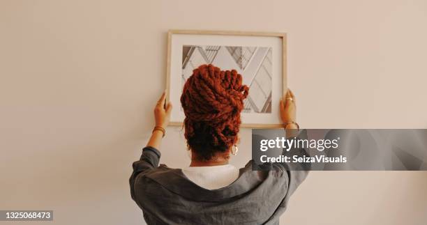 tiro de uma mulher irreconhecível pendurando uma pintura em casa - pendurando - fotografias e filmes do acervo