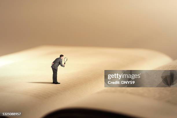 man on giant book with magnifying glass - big magnifying glass stock pictures, royalty-free photos & images