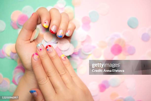 female hands with trendy colorful french manicure sprinkle many round paper confetti on a defocused pastel background, divided into light green and light pink part. copy space for your design. flat lay style - french manicure stockfoto's en -beelden