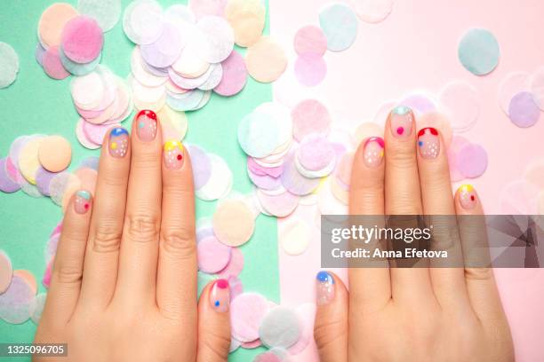 female hands with trendy colorful french manicure are lying on a pastel background, divided into light green and light pink part with many round paper confetti. copy space for your design. flat lay style - manicura de diseño fotografías e imágenes de stock