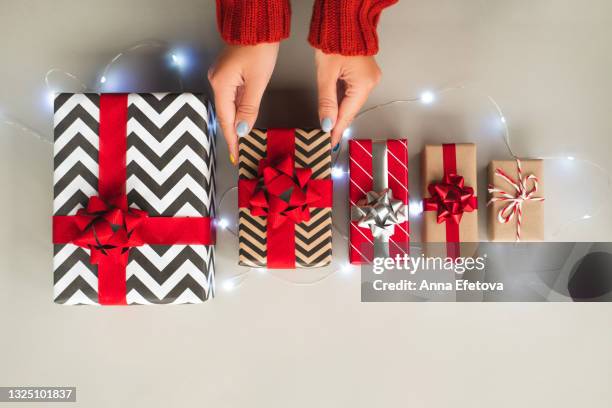 five different gift boxes on ultimate gray background with garland. hands of woman in red sweater are touching one of them. trendy colors of the year 2021. christmas celebration concept. top view. copy space for your design - multi year calendar stock pictures, royalty-free photos & images